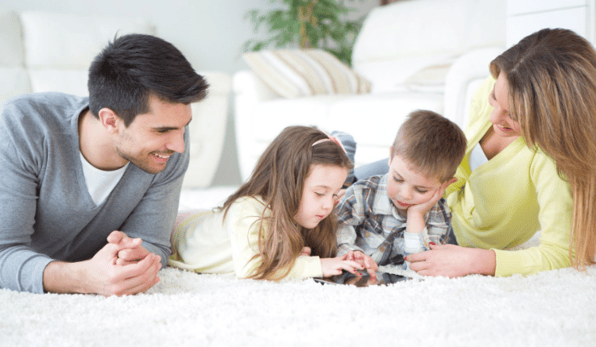 family of four with tow young children, all laying down as kids play on iPad, daycare waitlist